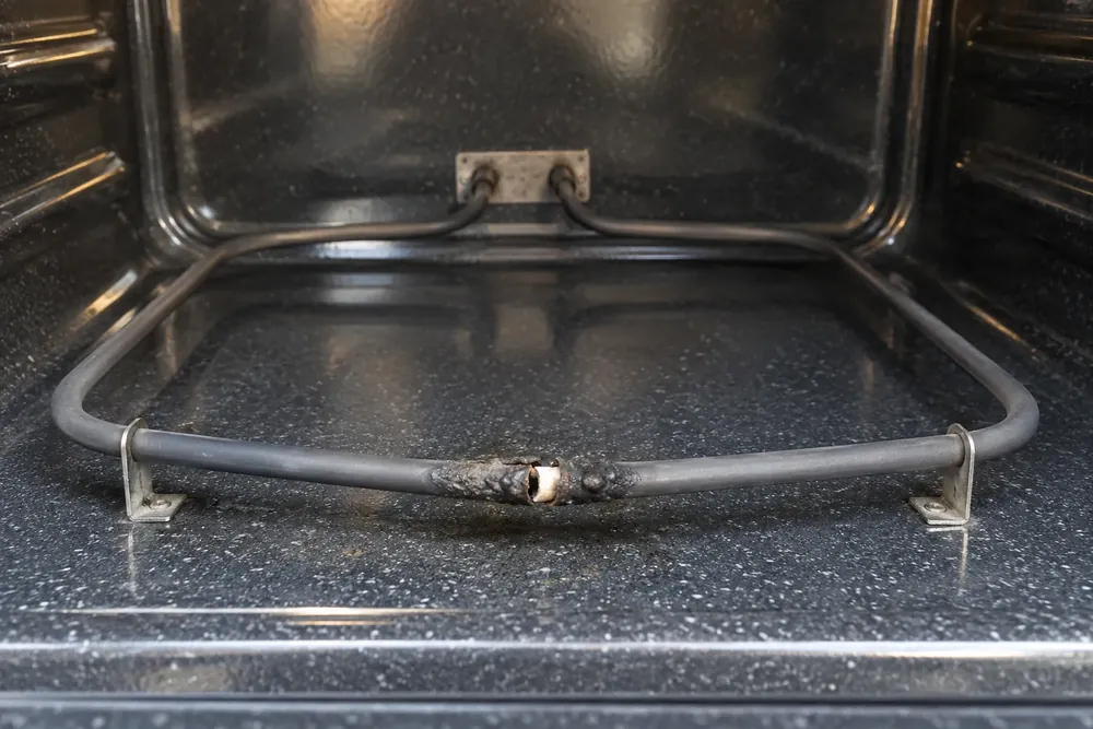 Blistered, broken section of a lower bake element inside an empty oven