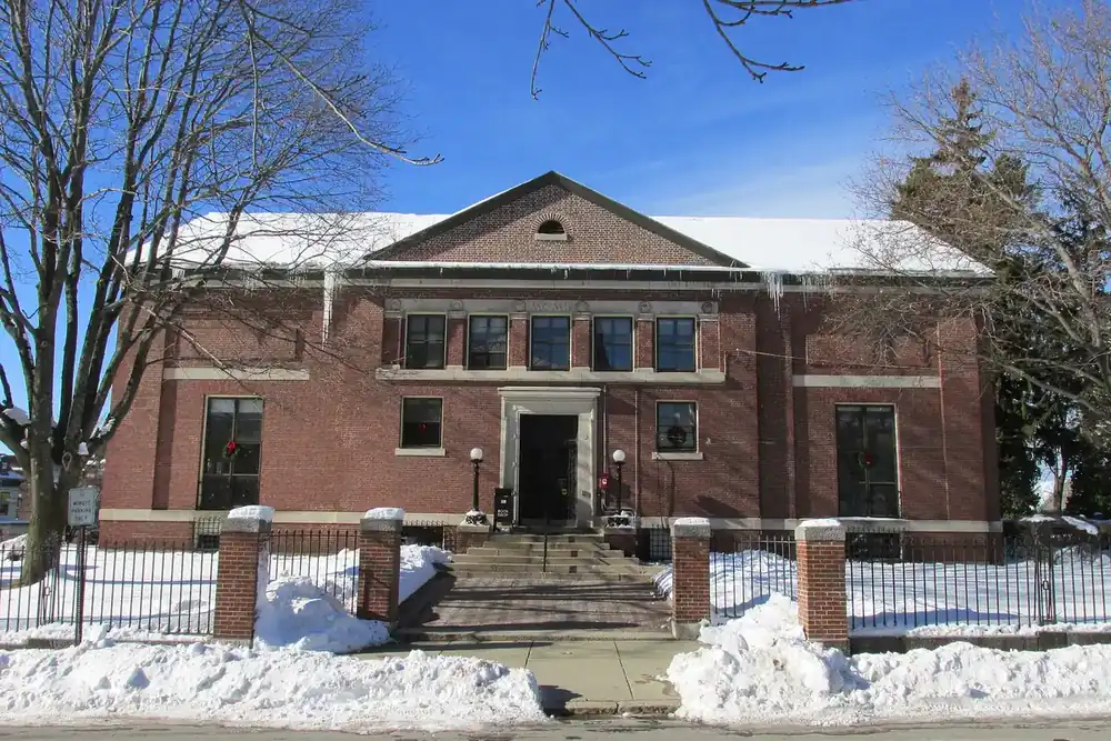 The brick Bigelow Library behind an iron fence after a snowfall in Clinton, Massachusetts