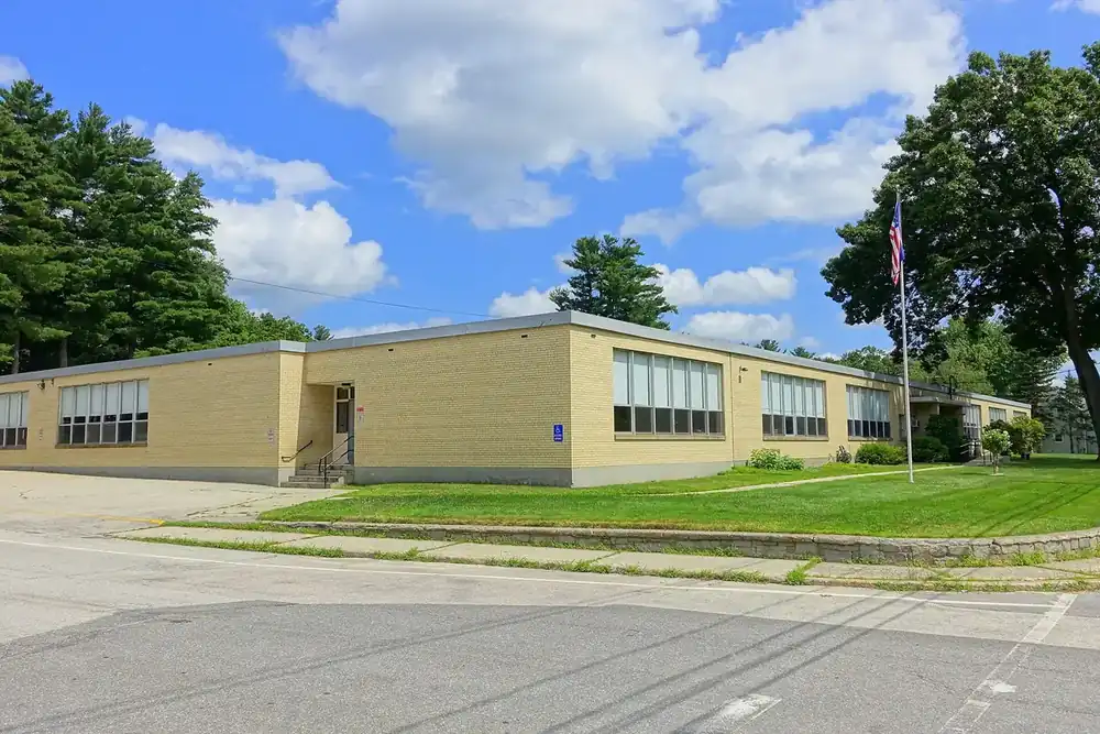 The tan brick Library Street School beside a lawn and flagpole in Hudson, New Hampshire