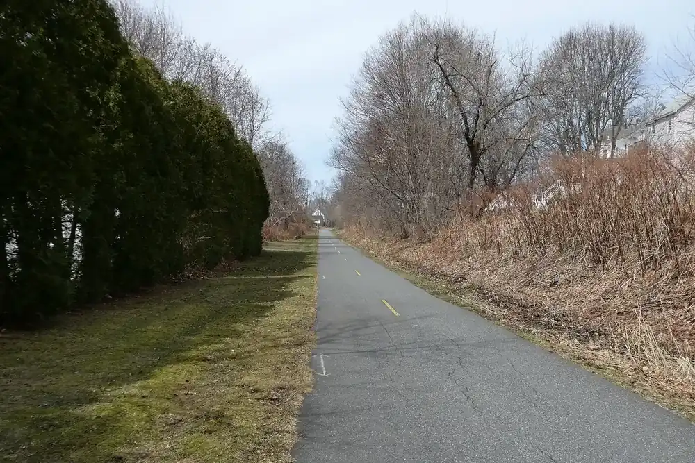The paved Assabet River Rail Trail lined with trees in Marlborough, Massachusetts