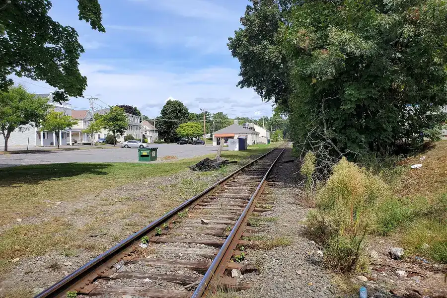 A rail line running past trees and low buildings in Northborough, Massachusetts