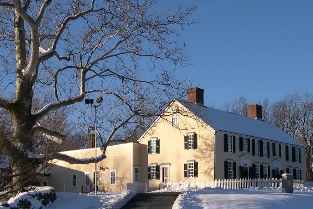 The historic Artemas Ward Homestead, a pale yellow colonial house, in winter in Shrewsbury